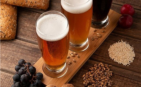 Три бокала пива с пеной на деревянной доске с хлебом, виноградом и зёрнами